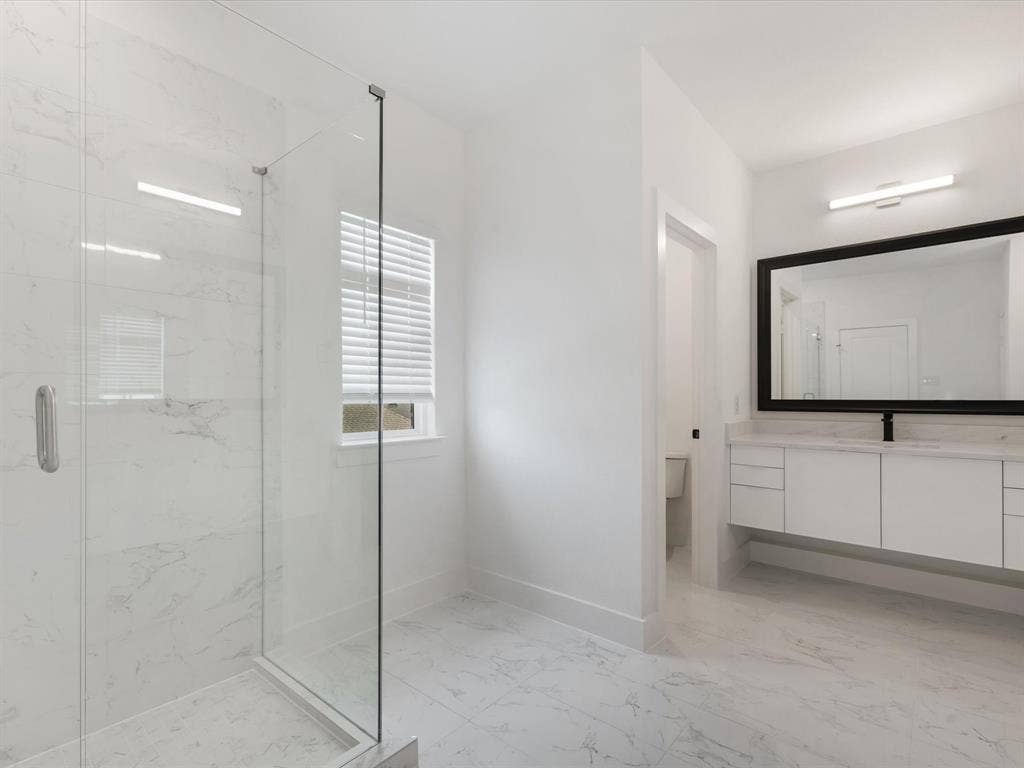 Primary Bathroom featuring light marble finish flooring, a marble finish shower, and vanity