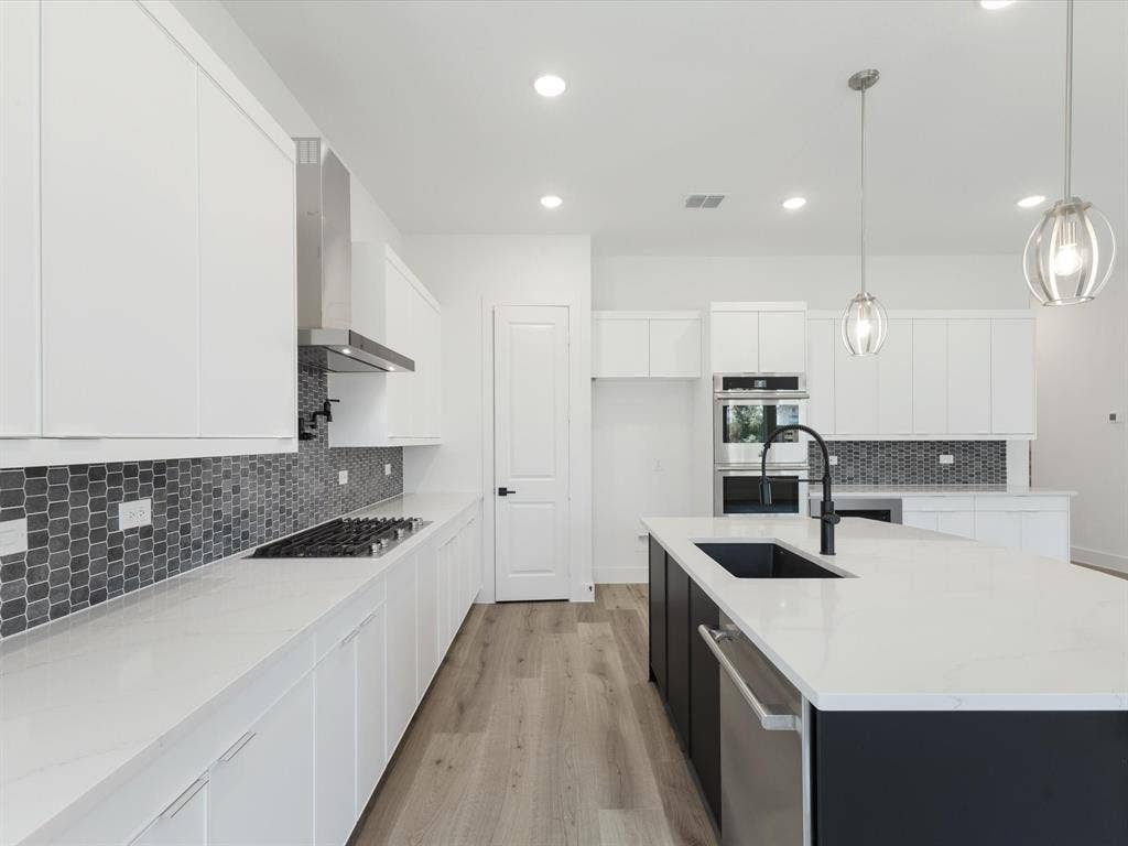 Kitchen with white cabinetry, backsplash, light stone counters, hanging light fixtures, and recessed lighting