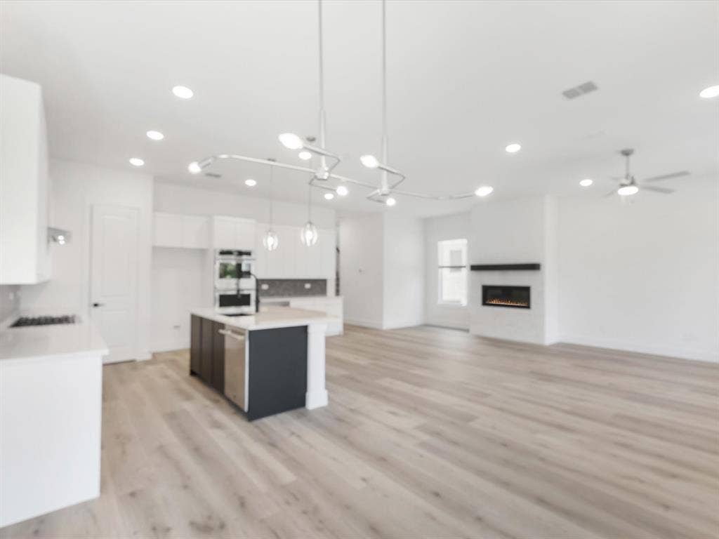 Kitchen with white cabinetry, open floor plan, a center island with sink, decorative light fixtures, and light wood-type flooring