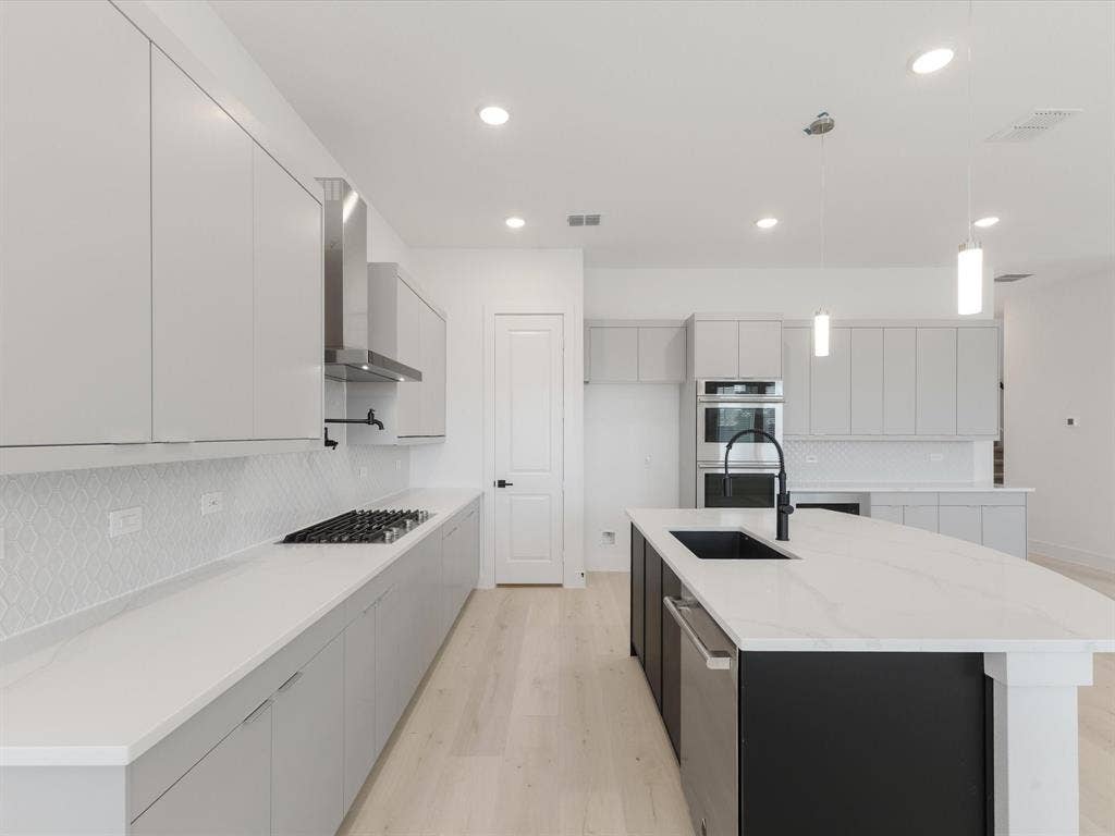Kitchen with tasteful backsplash, modern cabinets, hanging light fixtures, light wood-style flooring, and light stone countertops