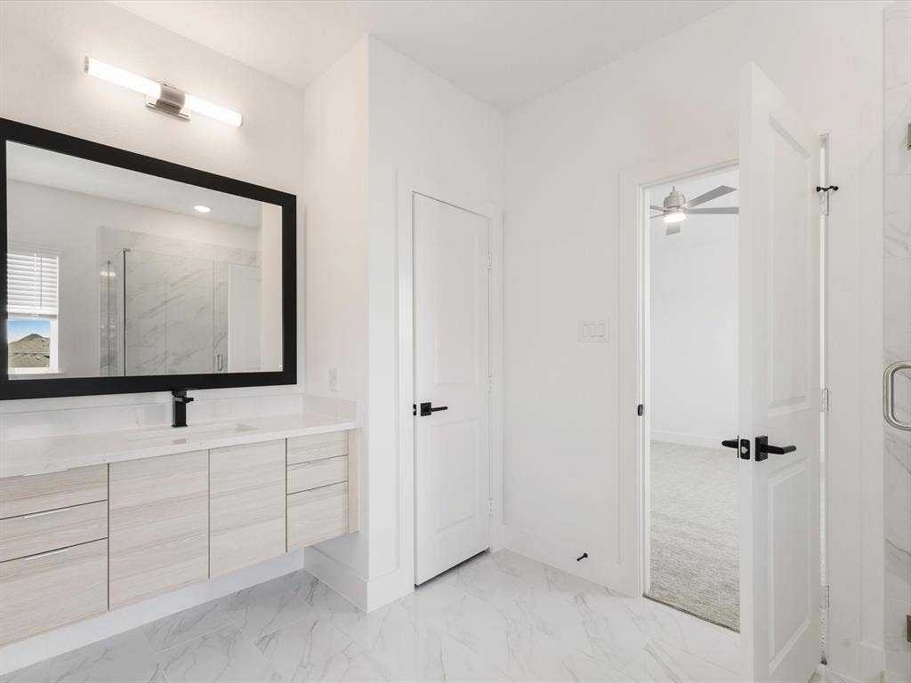 Ensuite primary bathroom with vanity, a marble finish shower, and light marble finish flooring