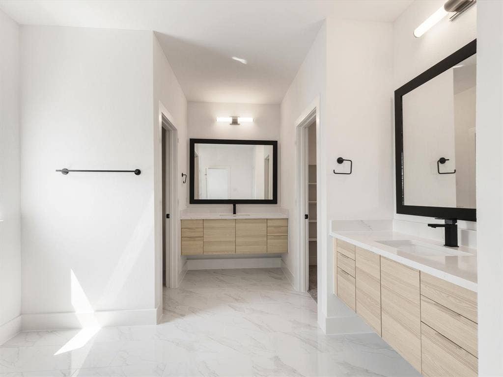 Ensuite primary bathroom with vanity, light marble finish flooring, and two sinks