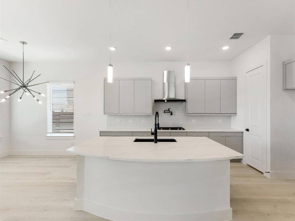 Kitchen with decorative backsplash, an island with sink, gray cabinetry, decorative light fixtures, and light wood-style flooring