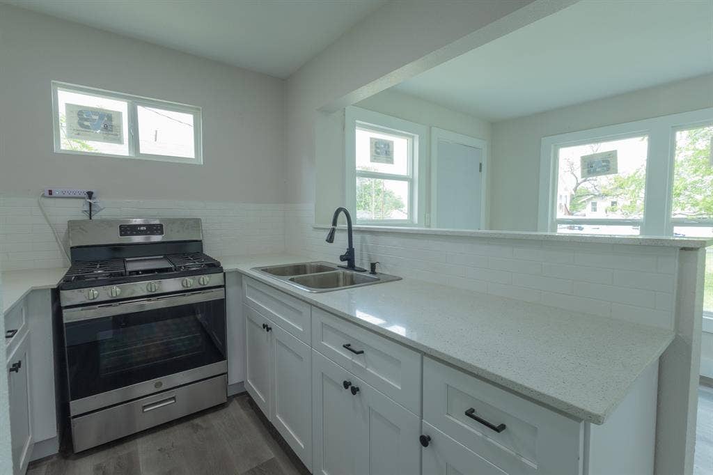1716 Ethel Avenue, #1714, 1718, 1720, Waco, TX 76707 Modern kitchen featuring stainless steel gas range with multiple burners, white cabinetry with hardware accents, quartz countertops, undermount sink with contemporary faucet, and abundant natural light from multiple windows