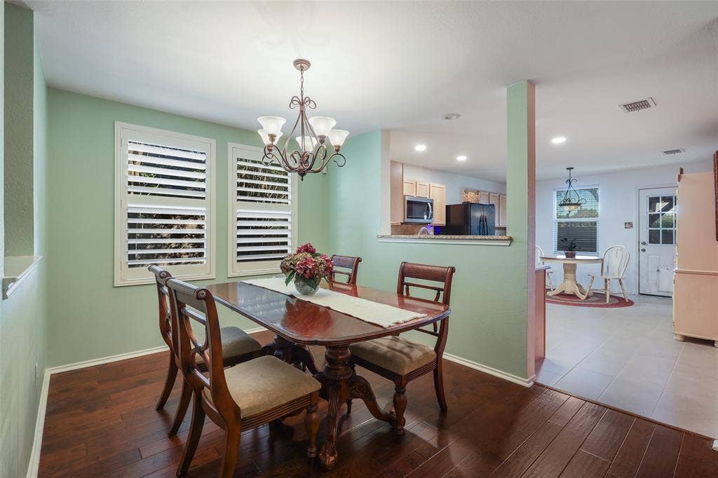 5409 Running Brook Lane, McKinney, TX 75071 Dining area featuring wood-finish flooring, two windows with plantation shutters, and an ornate chandelier