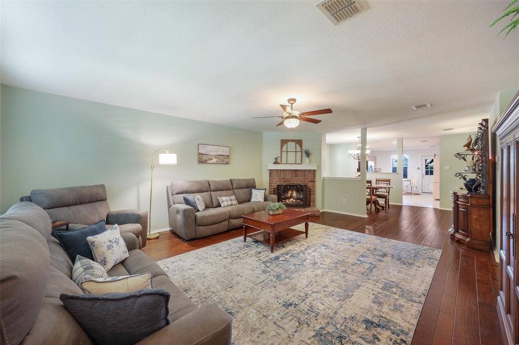 5409 Running Brook Lane, McKinney, TX 75071 Spacious living room with hardwood flooring, ceiling fan, and fireplace with brick surround