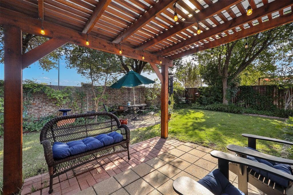 5409 Running Brook Lane, McKinney, TX 75071 Wood pergola with string lights, brick paver patio, brick perimeter wall, and a fenced yard with mature landscaping