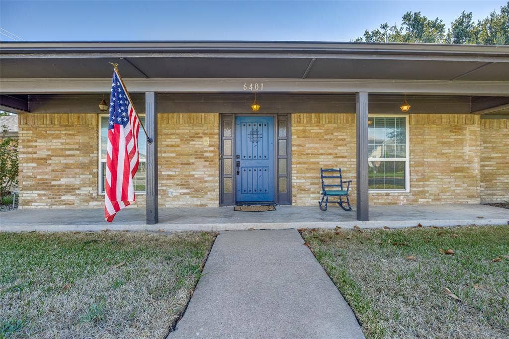 6401 Stonewall Street, Greenville, TX 75402 Brick exterior with a covered porch, blue entry door, and a concrete walkway