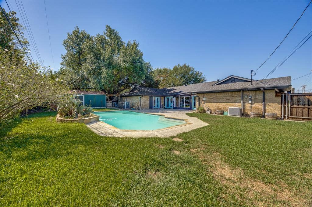 6401 Stonewall Street, Greenville, TX 75402 Expansive backyard featuring a swimming pool with a stone surround, a manicured lawn, and a brick-clad exterior