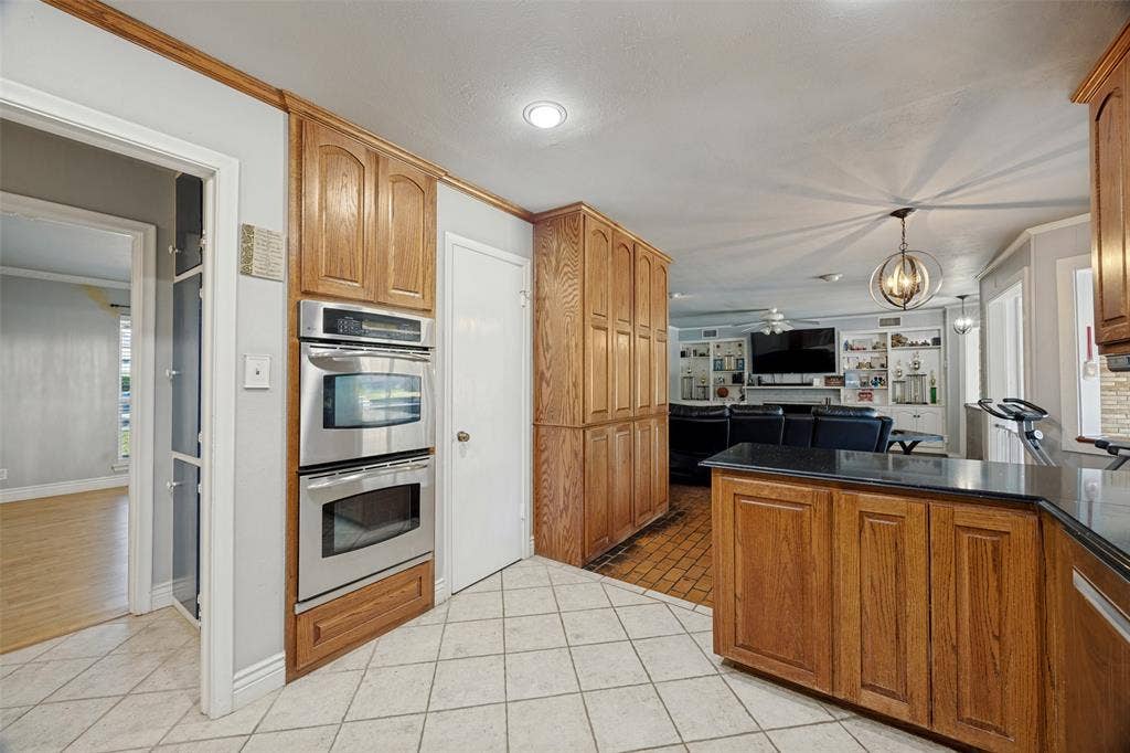 6401 Stonewall Street, Greenville, TX 75402 Kitchen featuring light-toned tile flooring, wood cabinetry, built-in stainless steel double ovens, and dark countertops