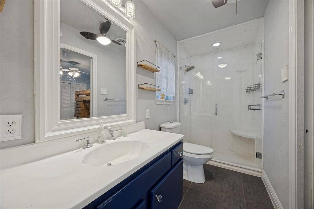 6401 Stonewall Street, Greenville, TX 75402 Built-in vanity with a white countertop and navy cabinetry, framed mirror, and a glass-enclosed shower with a built-in bench