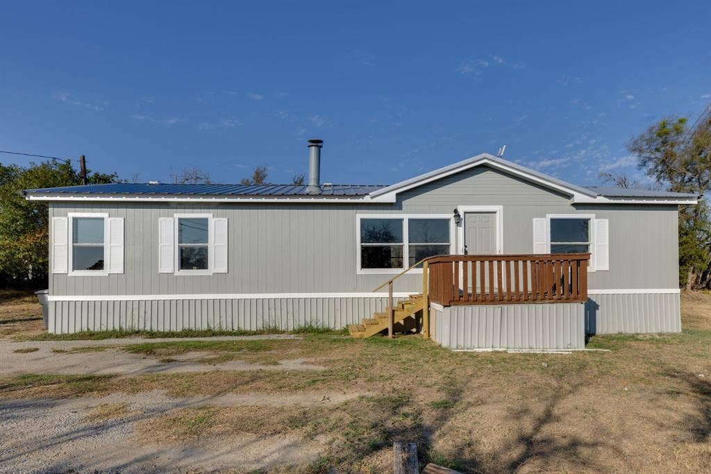 143 Summit Ridge Lane, Springtown, TX 76082 Light gray siding with white trim, metal roofing, white window shutters, and a wooden entry deck with steps