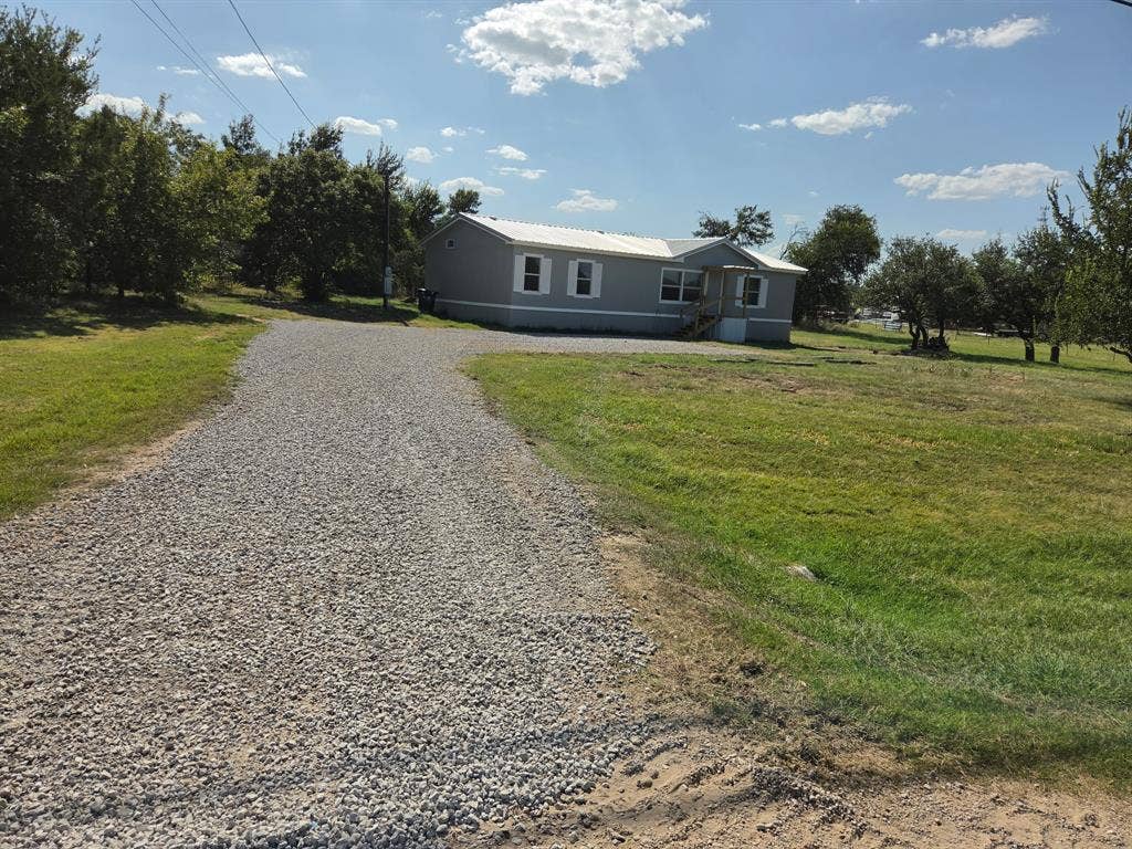 143 Summit Ridge Lane, Springtown, TX 76082 Gravel driveway leading to a single-story residence with gray siding and white trim