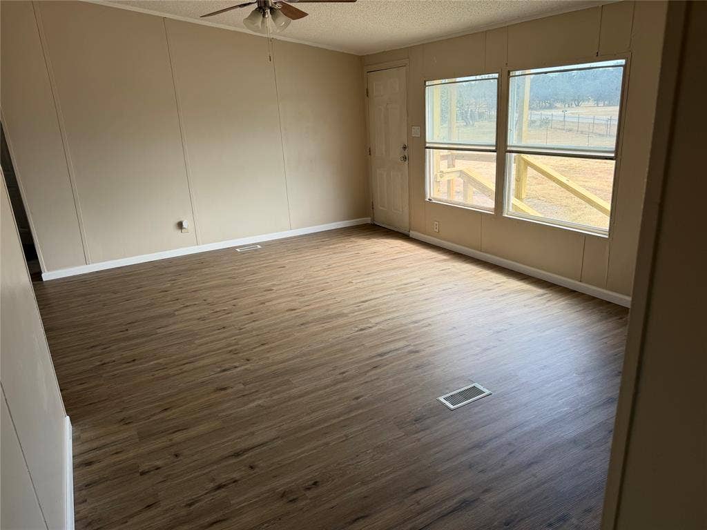 143 Summit Ridge Lane, Springtown, TX 76082 Spacious room featuring wood-finish flooring, two large windows, a ceiling fan, and a white paneled door