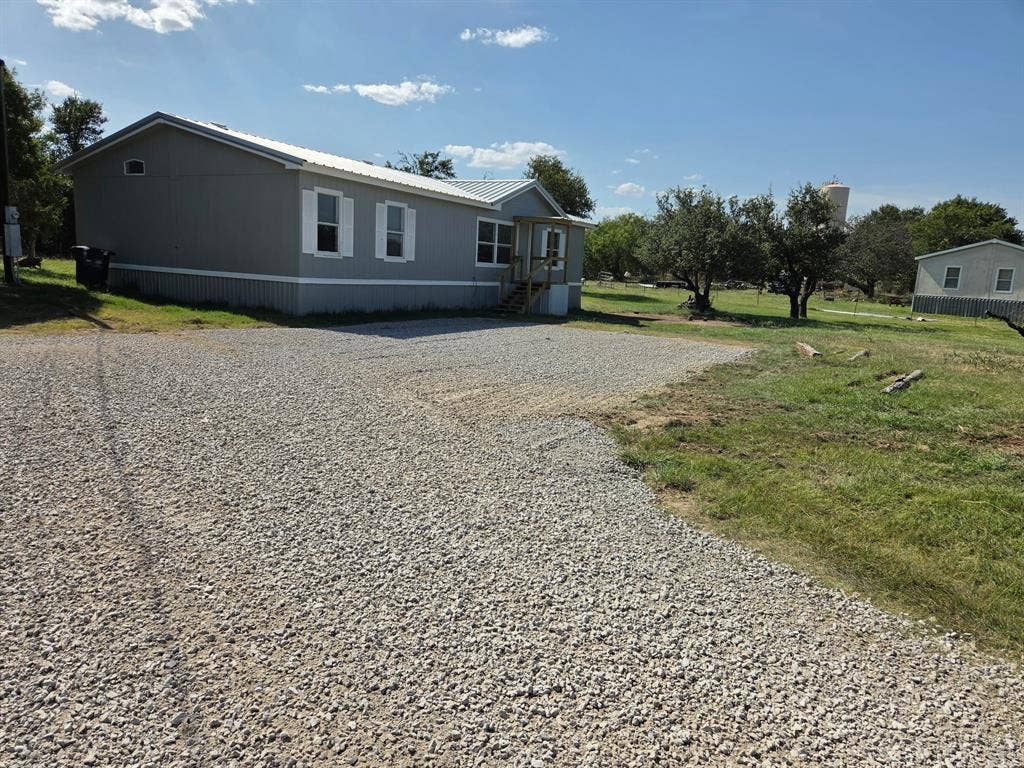143 Summit Ridge Lane, Springtown, TX 76082 Gravel driveway with a gray-sided home featuring white window shutters and a metal roof