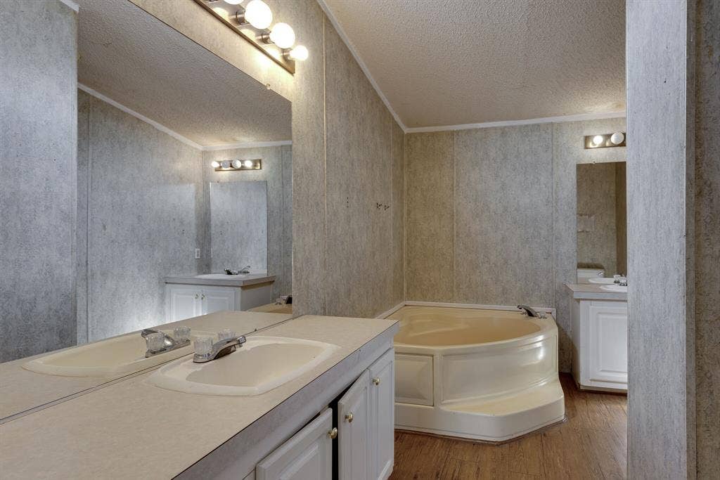 143 Summit Ridge Lane, Springtown, TX 76082 Dual vanity sinks with chrome fixtures, large wall-mounted mirror, built-in corner soaking tub, wood-finish flooring, and wall-mounted light fixtures