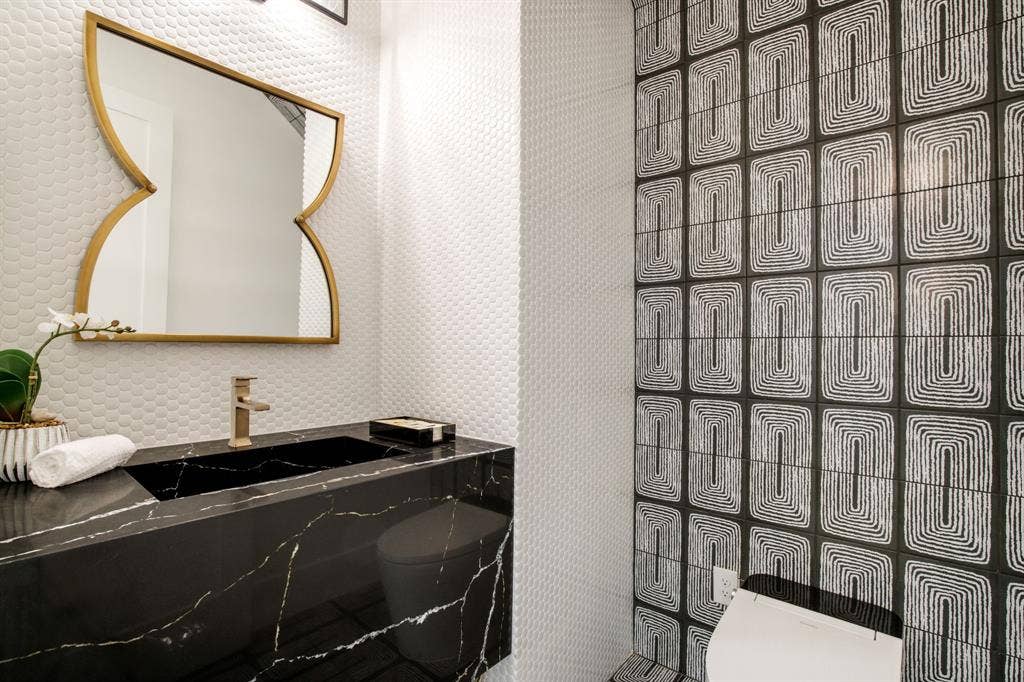 Black vanity with integrated sink, gold-finish faucet, and patterned wall tile