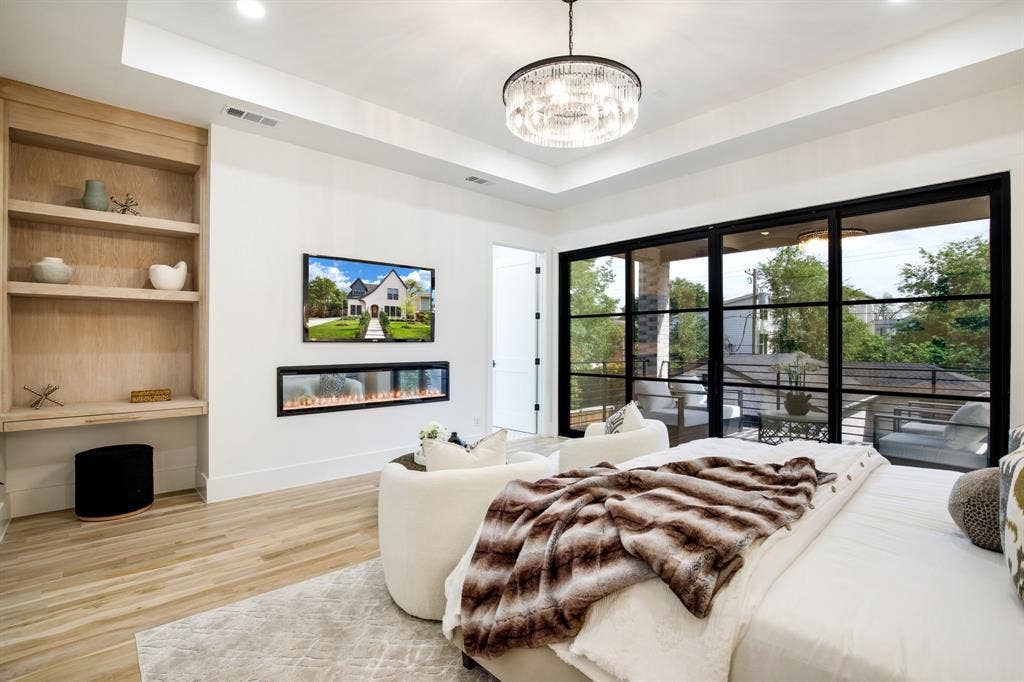 Recessed ceiling with a modern chandelier, built-in shelving, wall-mounted electric fireplace, and sliding glass doors to a private balcony