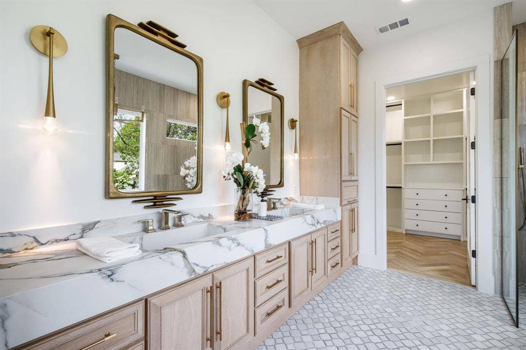 Double vanity with a marble-finish countertop, custom cabinetry, and brass fixtures