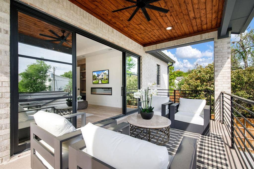 Covered outdoor patio with exposed wood plank ceiling, modern black ceiling fan, brick exterior, and dark metal railings