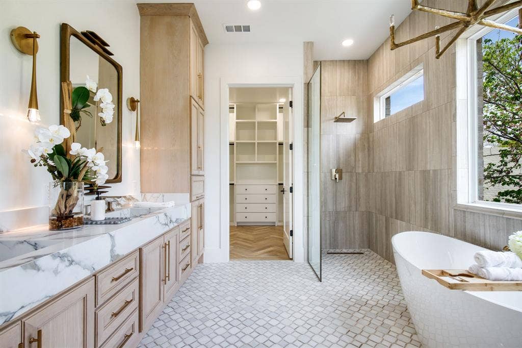Dual vanity with marble countertops and undermount sinks, freestanding soaking tub, glass-enclosed shower, and herringbone tile flooring in the closet