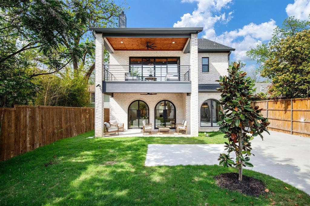 Dual-level outdoor living spaces, a covered upper balcony with a wood-finish ceiling, an expansive lower patio, arched window and door frames, and a brick exterior