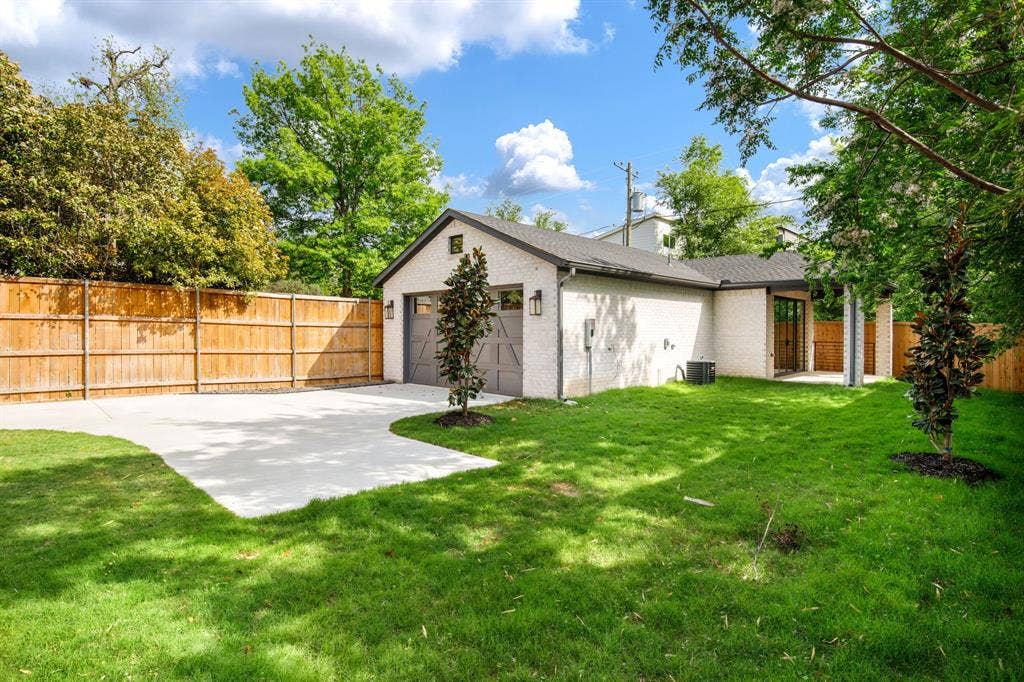 Expansive grassy yard with a concrete drive, privacy fencing, and a two-car garage