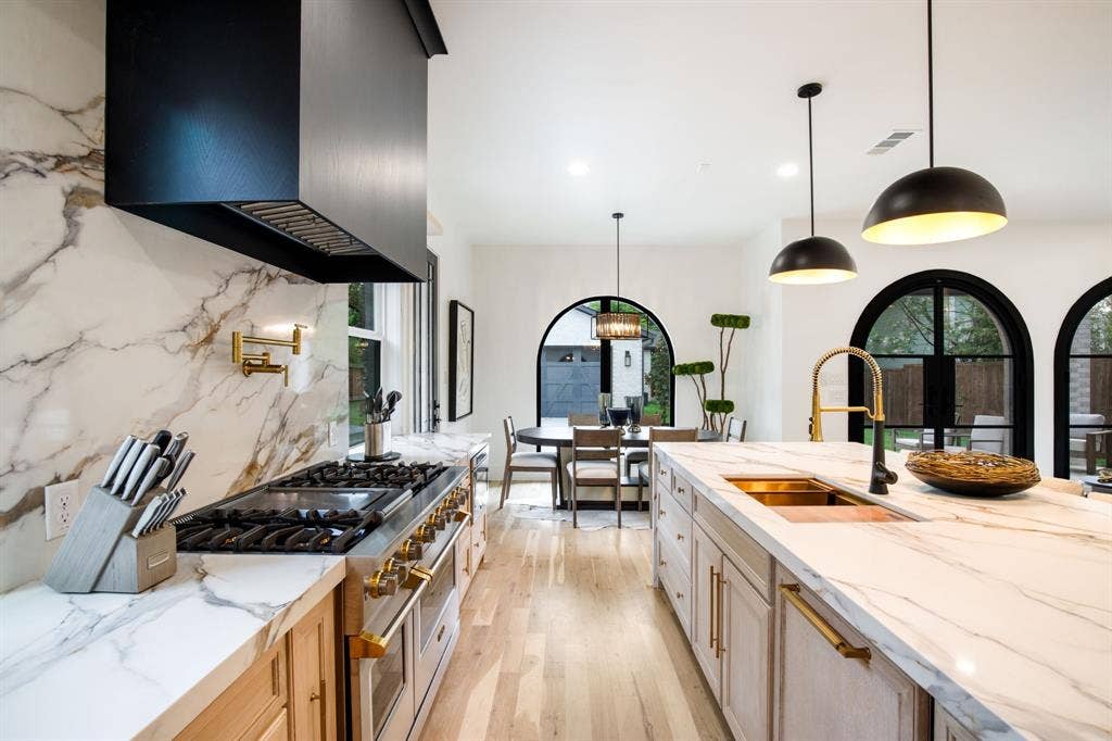 Gourmet kitchen with custom cabinetry, professional-grade range, full-height slab backsplash, central island, and arched windows