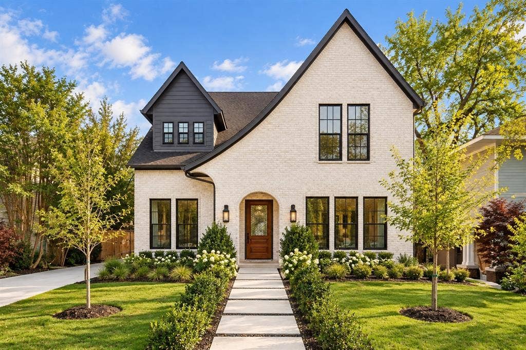 White brick exterior with dark trim accents, gabled roofline, dormer with siding, concrete walkway, and landscaped front yard
