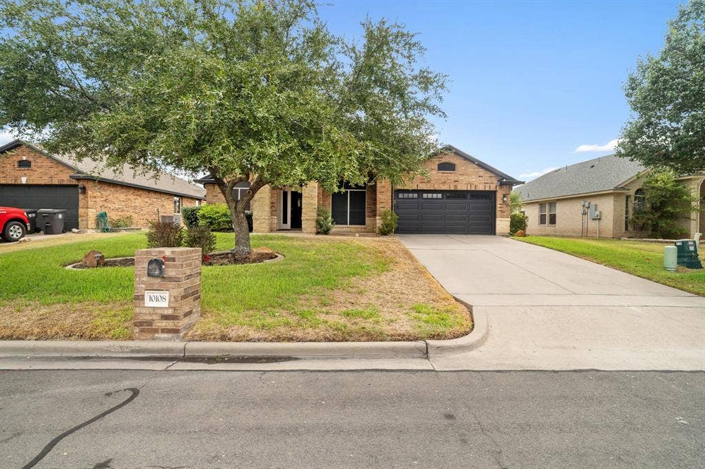 10108 Parker Springs Drive, Waco, TX 76708 Brick exterior home with an attached garage, concrete driveway, and a mature front yard tree