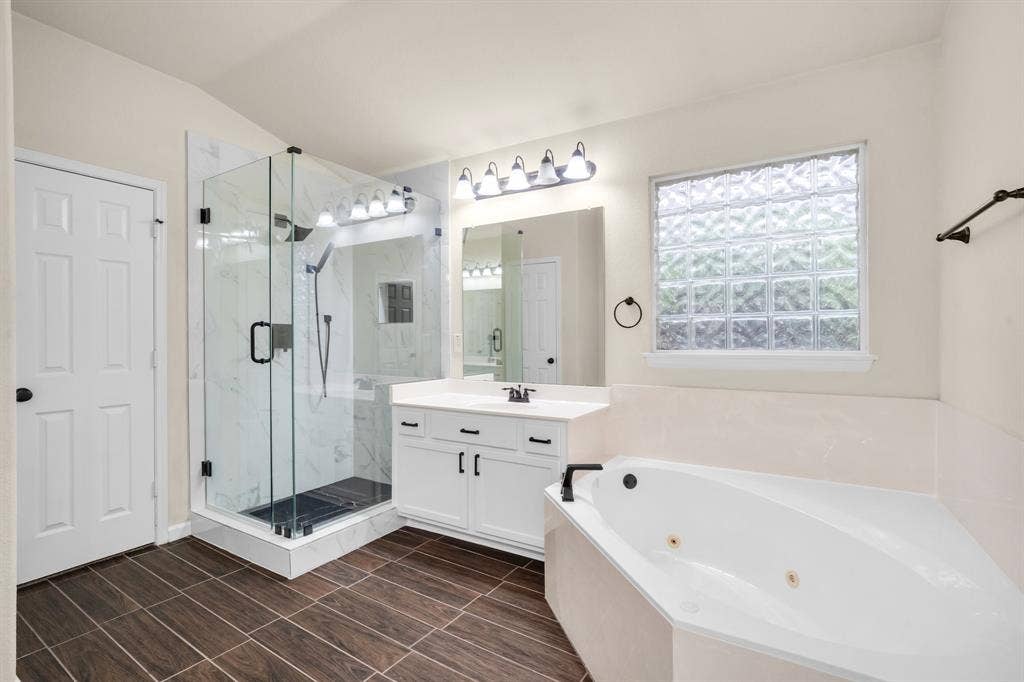 10108 Parker Springs Drive, Waco, TX 76708 Wood-finish flooring, glass-enclosed shower with tiled walls, white vanity with integrated sink, contemporary light fixture, and jetted corner tub