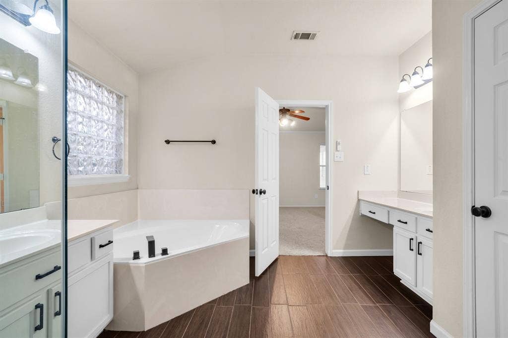 10108 Parker Springs Drive, Waco, TX 76708 Wood-finish flooring, corner soaking tub, dual vanities with white cabinetry, and a glass block window