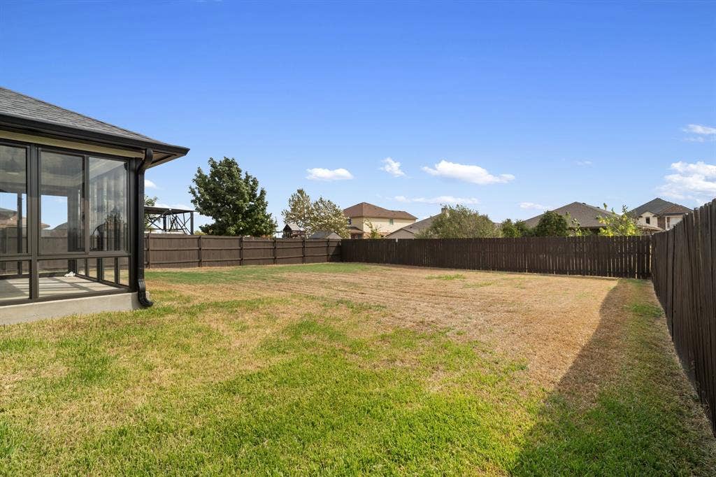 10108 Parker Springs Drive, Waco, TX 76708 Expansive fenced backyard featuring a sunroom addition with large glass panels, a dark wood privacy fence, and a large lawn area