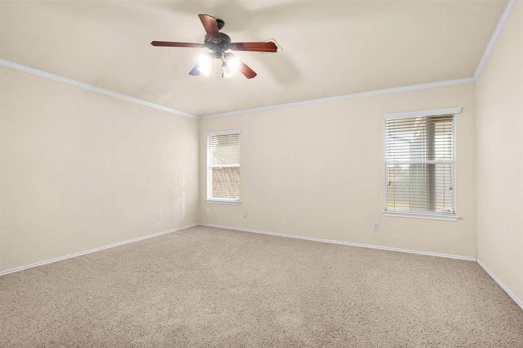 10108 Parker Springs Drive, Waco, TX 76708 Spacious room featuring neutral carpeting, crown molding, two windows with blinds, and a ceiling fan with integrated lighting