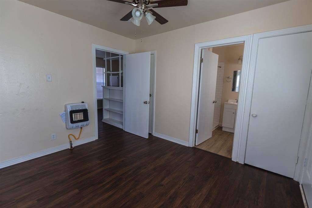 Wood-finish flooring, ceiling fan with integrated lighting, built-in shelving, white paneled doors, and a wall-mounted heater
