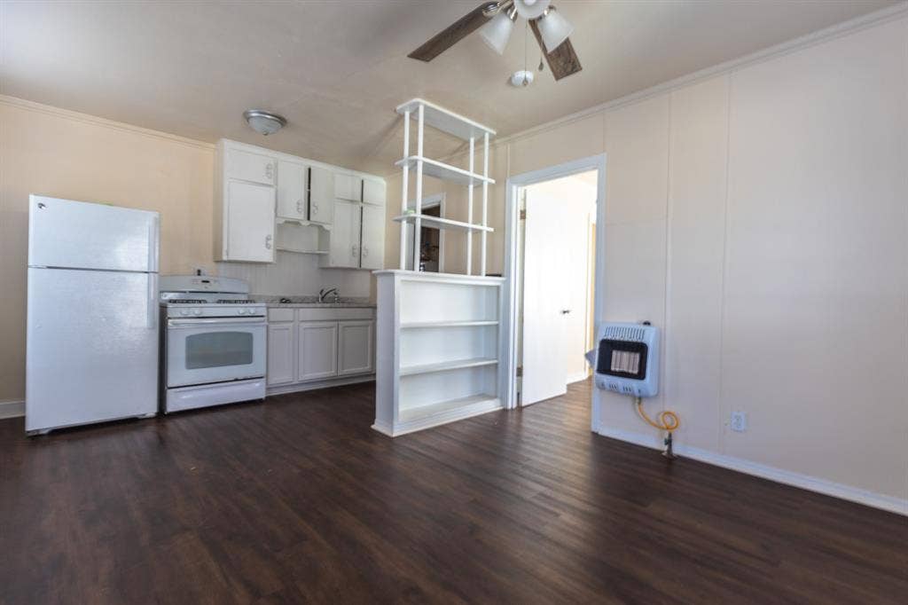 Open-concept kitchen and living area featuring stainless steel appliances, white cabinetry with upper glass-front storage, wood-finish flooring throughout, and abundant natural light from multiple windows