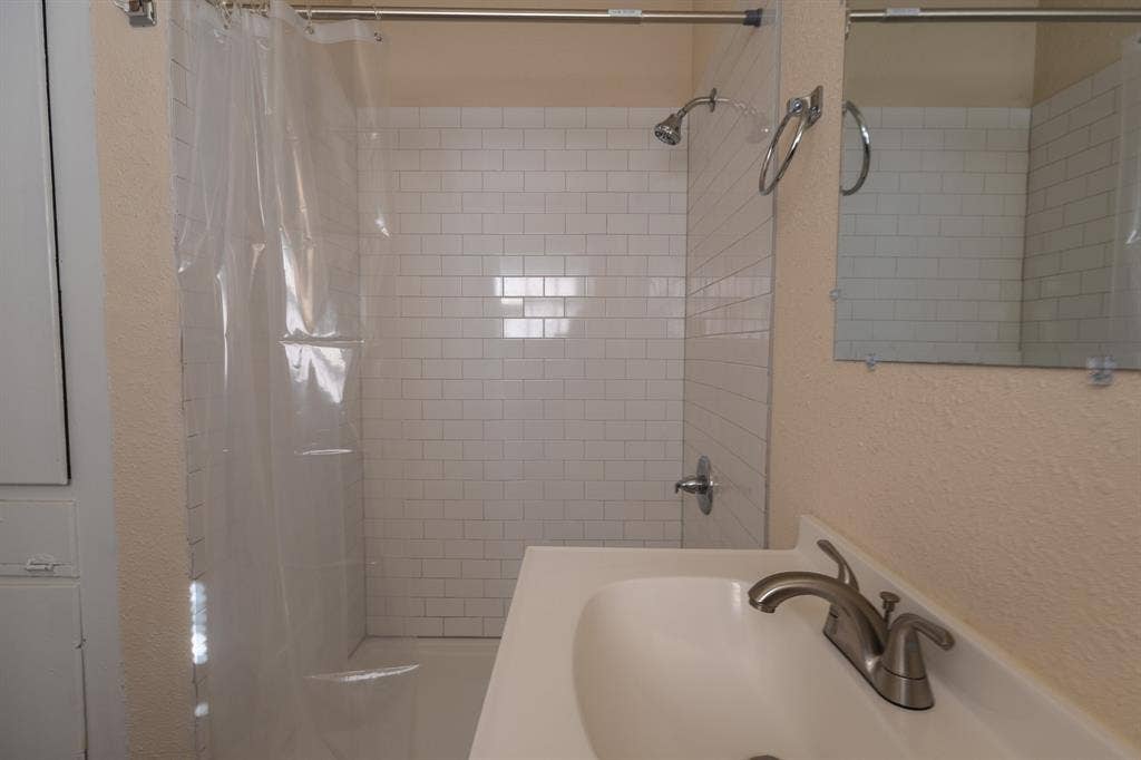 Bathroom featuring a shower with white subway tile surround, brushed nickel fixtures, a vanity with an integrated sink, and a wall-mounted mirror