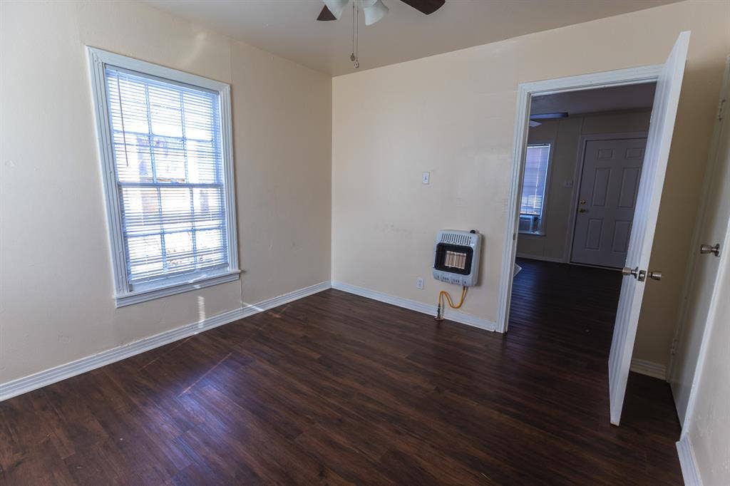 Bright corner bedroom featuring hardwood flooring, large double-hung window with plantation shutters, and neutral wall finishes