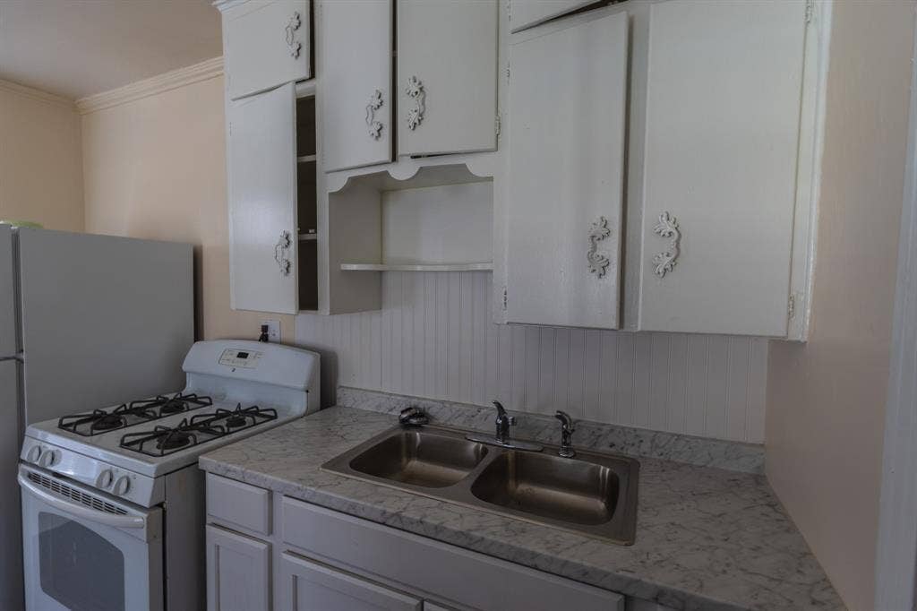 Kitchen featuring a double basin stainless steel sink, white cabinetry with decorative hardware, a gas range, and a refrigerator
