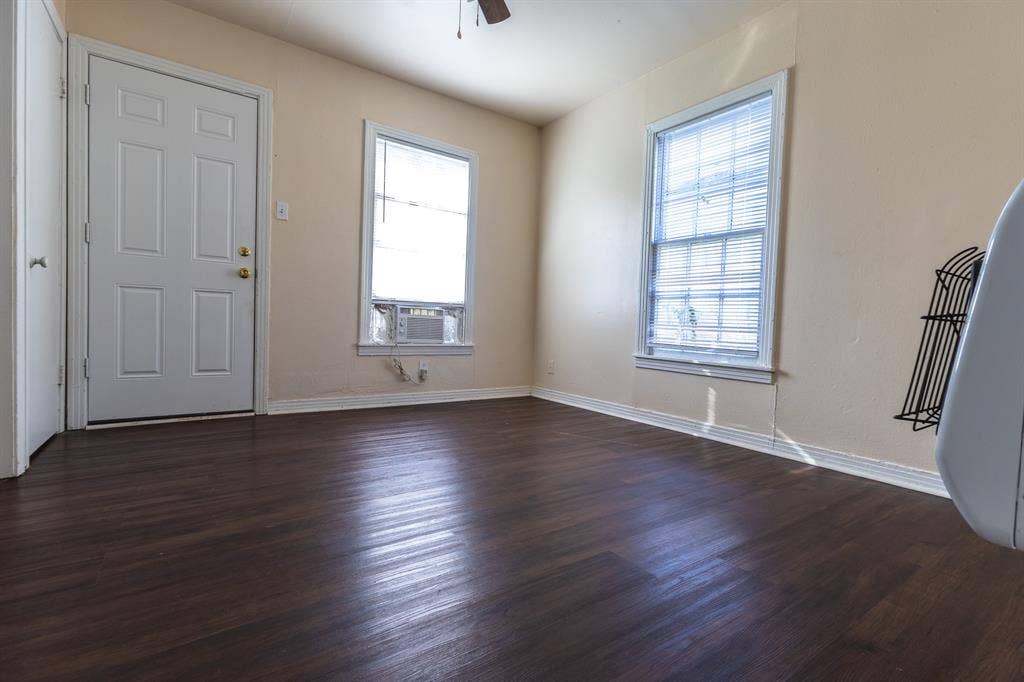 Wood-finish flooring, neutral wall tones, multiple windows with blinds, and an integrated window air conditioning unit