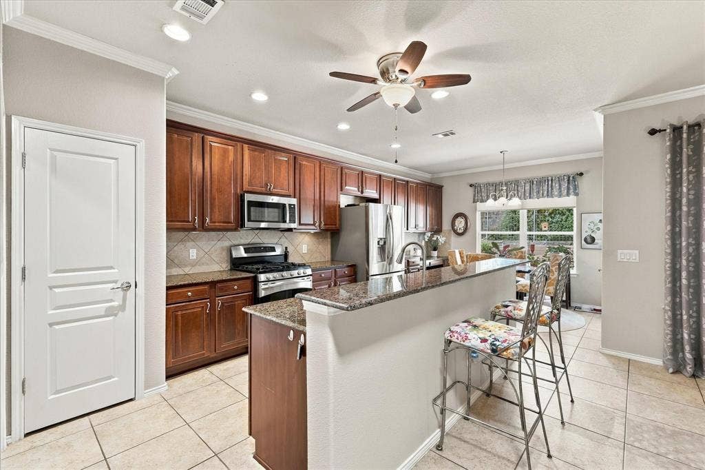 1118 Imperial Valley Lane, Frisco, TX 75036 Kitchen featuring wood cabinetry, stainless steel appliances, a breakfast bar with granite countertops, tiled flooring, and recessed lighting