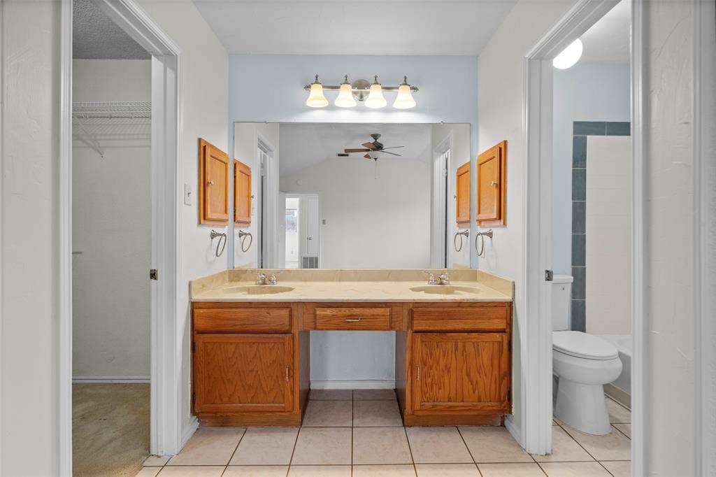 Double vanity featuring wood cabinetry, a dual-basin countertop, a full-width mirror, and four-light vanity fixture