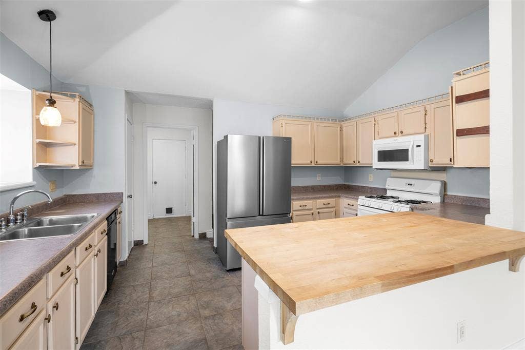 Kitchen featuring vaulted ceilings, light-tone cabinetry, butcher block countertop, stainless steel refrigerator, and pendant lighting