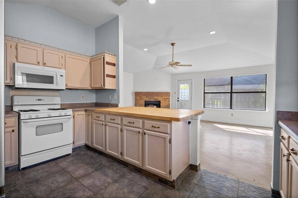 Kitchen featuring cabinetry with wooden countertops, a white gas range with overhead microwave, tiled flooring, vaulted ceilings, and a brick fireplace