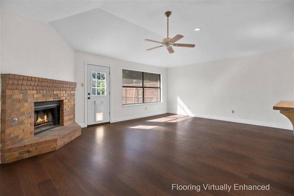 Vaulted ceiling with an integrated light fixture, wood-finish flooring, and a brick fireplace featuring a raised hearth