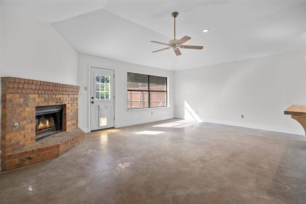 Vaulted ceiling, brick fireplace, polished concrete flooring, ceiling fan with light fixture, and exterior-access door