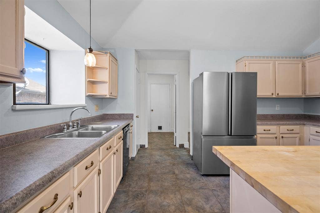 Kitchen featuring light-toned cabinetry, stainless steel refrigerator, stone-patterned countertops, a dual-basin sink with a gooseneck faucet, and tiled flooring