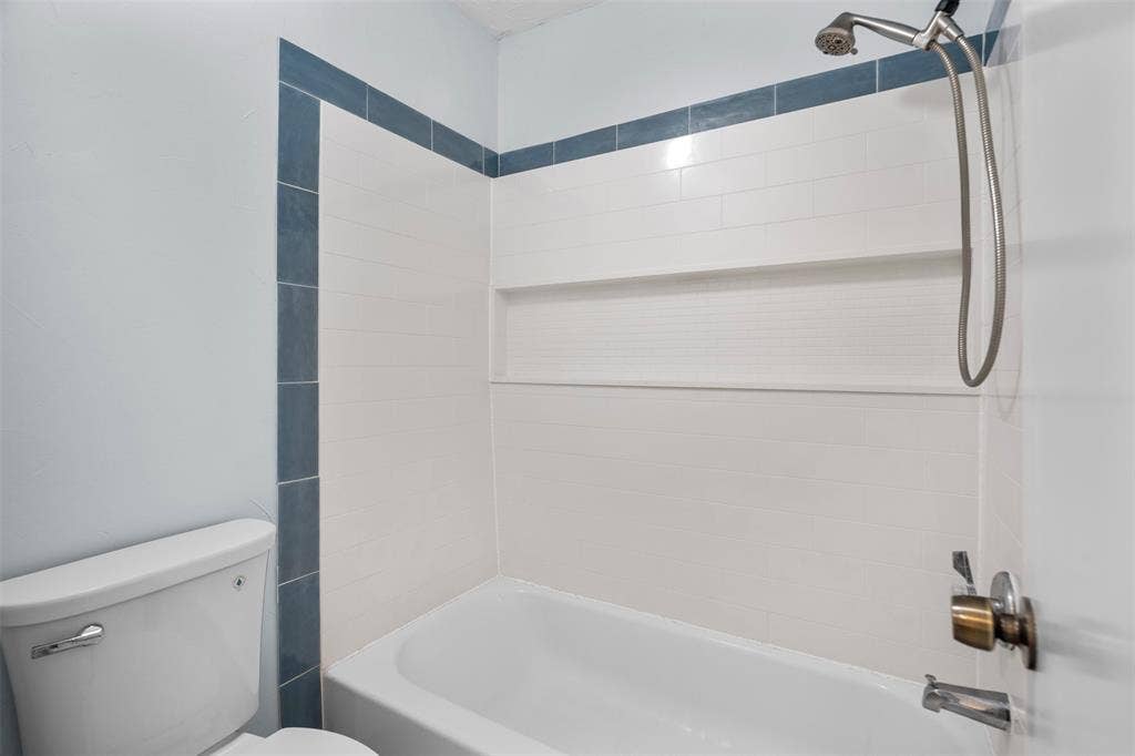Shower and tub combination featuring white rectangular wall tile with blue accent trim, integrated horizontal storage niche, and silver-tone handheld shower fixture
