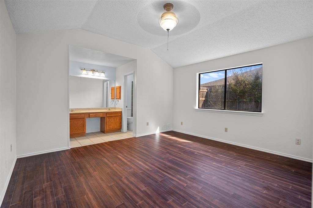 Vaulted ceiling, wood-finish flooring, and built-in vanity with dual sinks and large wall-mounted mirror