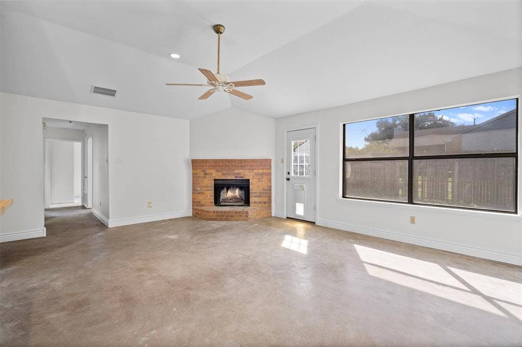 Vaulted ceiling with an integrated multi-blade ceiling fan, corner brick fireplace with a raised hearth, and large picture window